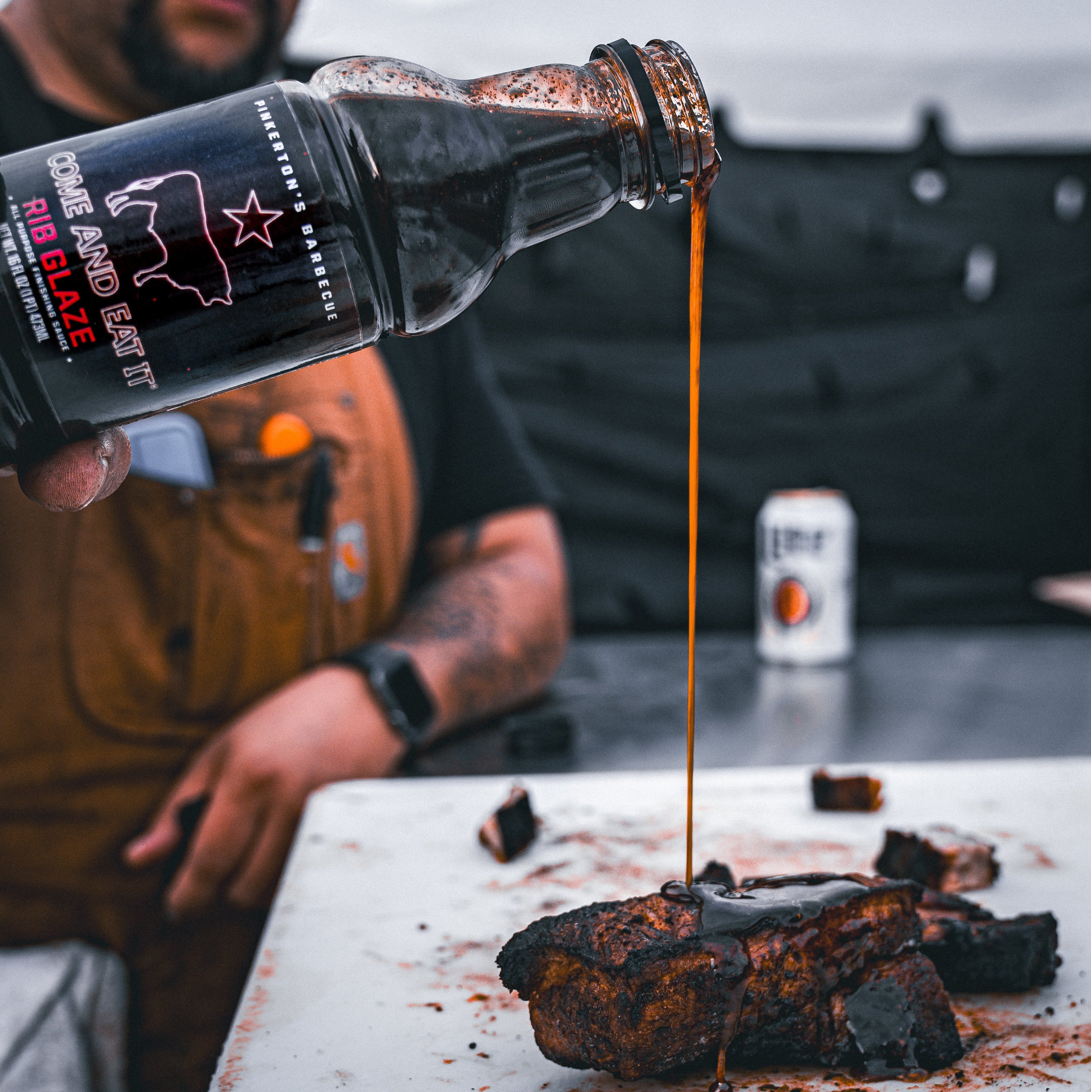 Chef pouring pinkertons rib glaze onto pork ribs at bbq competition